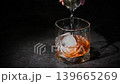 Bartender adding a portion of sugar syrup into a whiskey glass filled with ice and whiskey in an extreme close-up shot against a dark background. 139665269