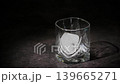 Large square ice cube being added into a whiskey glass in close-up against a dark moody background. Dramatic side lighting from left to right creates bright reflections on the glass  139665271