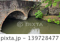 Rainy day on little old town canal with an old stone bridge, heavy spring rain falling on water surface with ripples and reflections of historic brick buildings under gloomy overcast sky 139728477