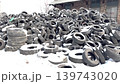 A large pile of old tires is shown at a recycling center. Workers are sorting through the tires for recycling purposes. The area is filled with rubber waste. This work impacts garbage management. High 139743020