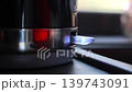 Finger Turning On Electric Kettle Switch In Kitchen, close up home video frame with red indicator light and soft window glow 139743091
