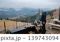 Man Grilling Meat In Mountain Valley Landscape, outdoor barbecue video frame with smoke, wooden table and misty hills behind 139743094