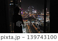 Woman silhouette looking at night skyline from hotel window, travel video frame with illuminated towers and city lights 139743100
