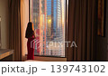 woman in red dress looking out from hotel window, travel video frame with sunset reflections and high city towers 139743102
