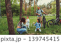 Family with children exploring forest park, mother taking photo of kids while father stands with bicycles nearby enjoying time together 139745415