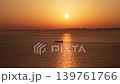 A cargo ship sails across the ocean, glowing in the setting sun. 139761766