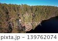 Dynamic FPV drone orbit reveal over Kolmoislampi lake surrounded by pine forest and rocky wilderness in Nuuksio, Finland. 139762074
