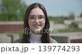 Close-up portrait of a young white female student wearing glasses with long dark hair in a park 139774293