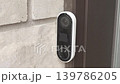 Security camera mounted on a wall captures the entrance area, showcasing the device's design and installation on a textured stone surface 139786205