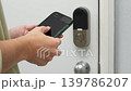 Person using smartphone to unlock smart door lock with visible screen interface and modern door hardware in a residential setting 139786207