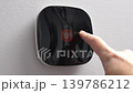 Hand adjusts smart thermostat display showing temperature settings in a modern home environment with a clean wall background 139786212