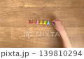 A child's hands reach for a light blue clip from a wood-grain desk; silent, 4K slow motion. 139810294