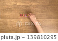 A child's hands picking up a yellow paperclip from a wood-grain desk; silent, 4K slow motion. 139810295