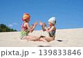 Cute playful girls in swimsuits are playing palm games with each other, sitting on the hot sand of the beach on the coast 139833846