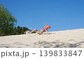 A cute girl in a swimsuit and sunglasses, with a scarf tied on her head to protect her from the sun's rays. Relaxing on a sandy beach on vacation 139833847
