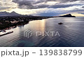Moody coastal panorama at twilight, dramatic brooding clouds and sun glint on water, solitary islet near quiet 139838799