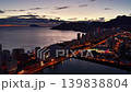 Dusk coastal skyline with illuminated boulevard and ocean soft sunset hues, calm water, glowing traffic 139838804