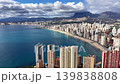 Aerial turquoise bay and skyline with highrise buildings lining sandy beach under dramatic clouds, mountain 139838808