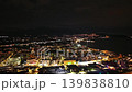 Night aerial harbor lights over city, glowing waterfront and marina reflections on calm bay, distant hills 139838810