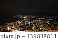 Night aerial bay lights over coastal town, shoreline illuminated by street grid, distant pier lights 139838811