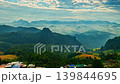 Stunning aerial panorama of Baan Jabo featuring a sea of mist, lush highlands, and tranquil rural life beneath a colorful sunrise sky. Aerial View of  Sun Rays Over Rural Mountain Landscape 139844695