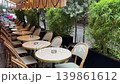 Empty terrace of Parisian cafe on spring rainy day, lush green plants surround tables and chairs on wet cobblestone streets, no people at tables covered with rainy water, cozy, atmospheric view 139861612