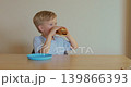 Close-up of a young boy holding a kids burger in his hands and smelling it with appetite. Fast food as a part of children nutrition. 139866393