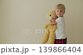 White boy hugging yellow teddy, minimalist beige wall background, red plaid pajama pants, soft plush squeezed close, gentle facial expressions alternating 139866404