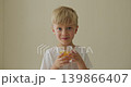 Happy kid in bright room, Young boy enjoys his glass of orange, Shy child in minimalist setting tastes fresh orange juice and smile 139866407