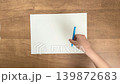 A child's hands (overhead view) placing a light blue pen on a blank sheet of paper. 139872683