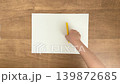 A child's hand holding a yellow pen placed on a blank sheet of paper (overhead view). 139872685