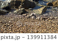 Waves hit the shore at Villajoyosa as stones sit among sand. The clear water reveals patterns of movement and texture on the beach. Nature creates a simple view of the coast. 139911384