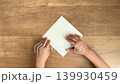 A child's hand, supported by an adult's hand, folds a yellow origami paper into a triangle. 139930459