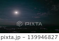 Aerial timelapse of moon over mountains with city lights below, clouds moving across night sk 139946827