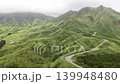 Aerial footage of a mountain road winding through the green volcanic hills of Minami Aso, Kumamoto Prefecture. 139948480