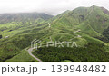 Aerial footage of a mountain road winding through the green volcanic slopes of Minami Aso, Kumamoto Prefecture. 139948482