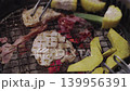 Close-up of Japanese yakiniku BBQ with meat slices, corn, and pumpkin grilling on a charcoal wire mesh. Metal tongs flipping meat in a restaurant setting. Traditional Asian cuisine concept. 139956391