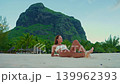 A beautiful girl with a beautiful figure in a white swimsuit sits relaxed on the beach sunbathing and admiring the ocean. Mauritius 139962393