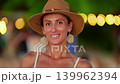 A young woman in a straw hat on vacation near the ocean looks at the camera and smiles serenely 139962394