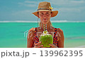 A close-up portrait of a woman drinking a fresh coconut cocktail with turquoise water on the shore of the Indian Ocean. A smile on the face. Positive emotions. Concept of relaxation and travel 139962395