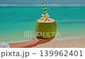 A close-up portrait of a woman drinking a fresh coconut cocktail with turquoise water on the shore of the Indian Ocean. A smile on the face. Positive emotions. Concept of relaxation and travel 139962401