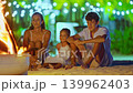 A mother and her children sit near a beautiful fire pit on the ocean shore enjoying the evening atmosphere during vacation and holidays 139962403