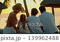 A family of four sits at a beautiful sunset on the ocean shore and takes a photo. Concept of family vacation and time together 139962488