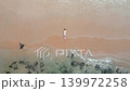 Aerial top down view of woman standing on tropical sandy beach near clear sea water and rocks during sunny summer vacation. 139972258