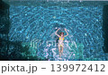 Top down drone view of woman floating in blue swimming pool during sunny tropical holiday and luxury resort relaxation. 139972412