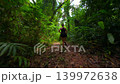 Woman running through dense tropical rainforest trail surrounded by lush jungle vegetation and tall trees in Southeast Asia. Active adventure and fitness travel concept in wild nature. 139972638