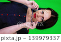 Woman holding glasses in hands standing in front of a green chroma key screen. Studio portrait for video editing and background replacement. 139979337