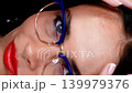 Closeup of a woman's face wearing blue glasses on a green screen. Detailed macro shot of eyes and makeup for optics advertisement. 139979376