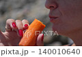 Woman eating carrot, healthy snack outdoors close-up 140010640