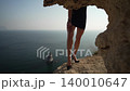 Legs, cliff, sea. Slender female legs in black high heels and a short dress standing dramatically on a rocky cliff edge overlooking the blue ocean. 140010647